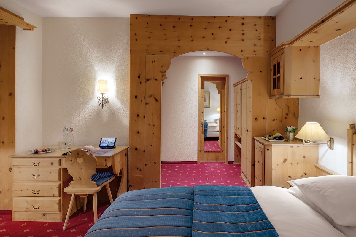 Ett hotellrum med ett skrivbord i trä, en säng med ett blått överkast, en sänglampa och ett rött heltäckningsmatta på golvet.
