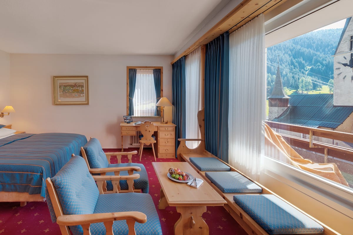 Ett hotellrum med två sängar, ett skrivbord, en stol, ett bord och ett fönster med utsikt över ett berg.