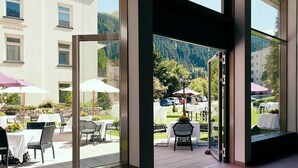 An outdoor dining area with tables and chairs, a view of a parking lot, and a mountain backdrop. - Morosani Schweizerhof (Davos)