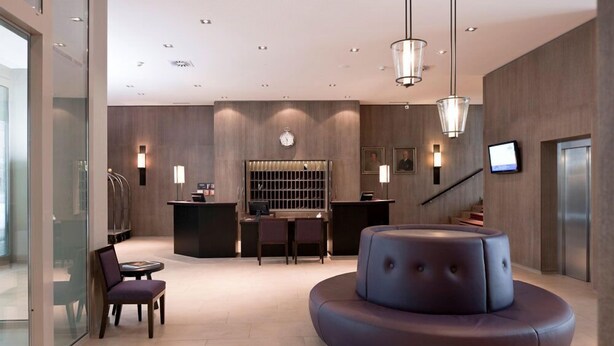 A modern lobby with a reception desk, seating area, and a staircase. - Morosani Schweizerhof (Davos)