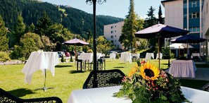 An outdoor dining area with tables and chairs, umbrellas, and a mountain backdrop. - Morosani Schweizerhof (Davos)