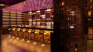 A bar area with multiple stools, a well-lit shelf with bottles, and decorative hanging lights.