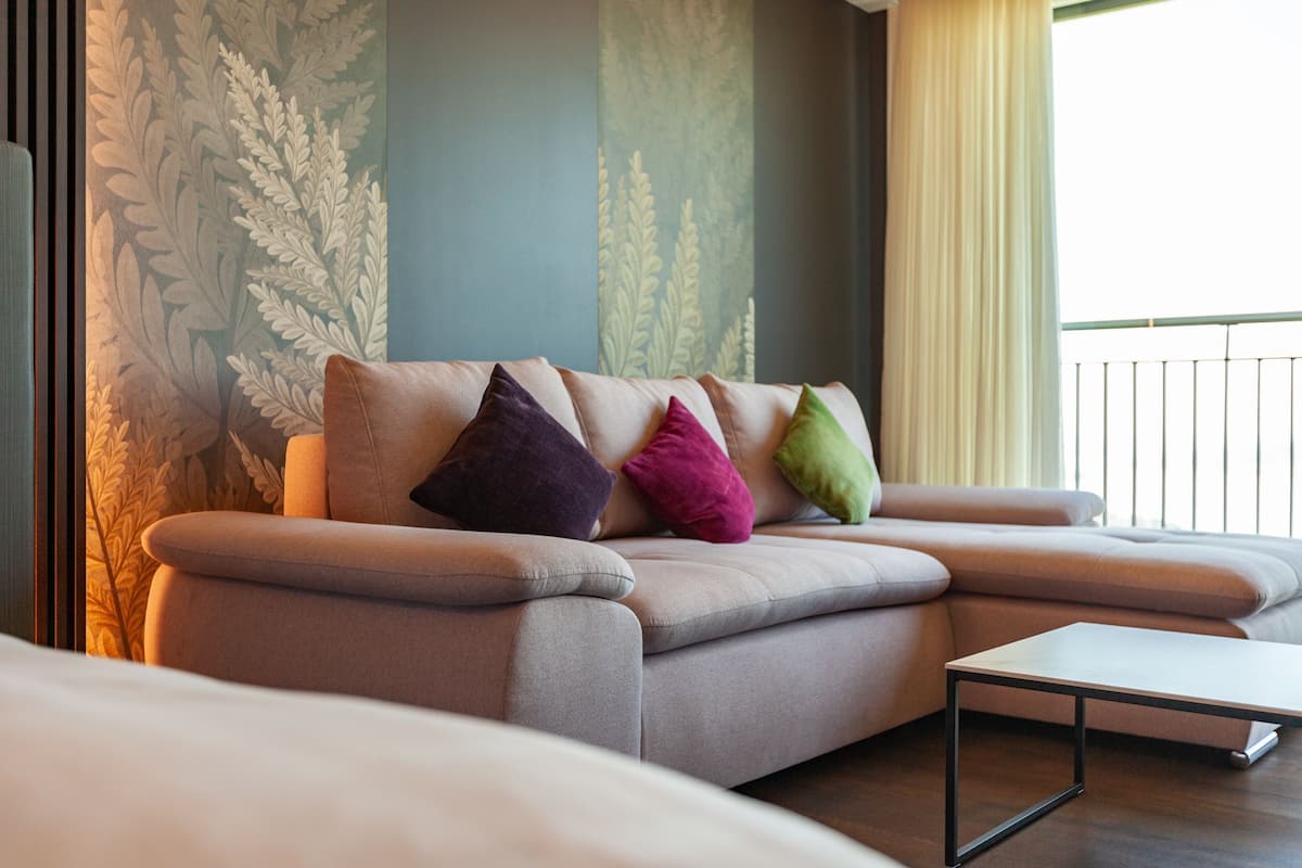 Ein modernes Wohnzimmer mit einer Couch, bunten Kissen, einem Couchtisch und einer Wand mit einem Blattmuster.