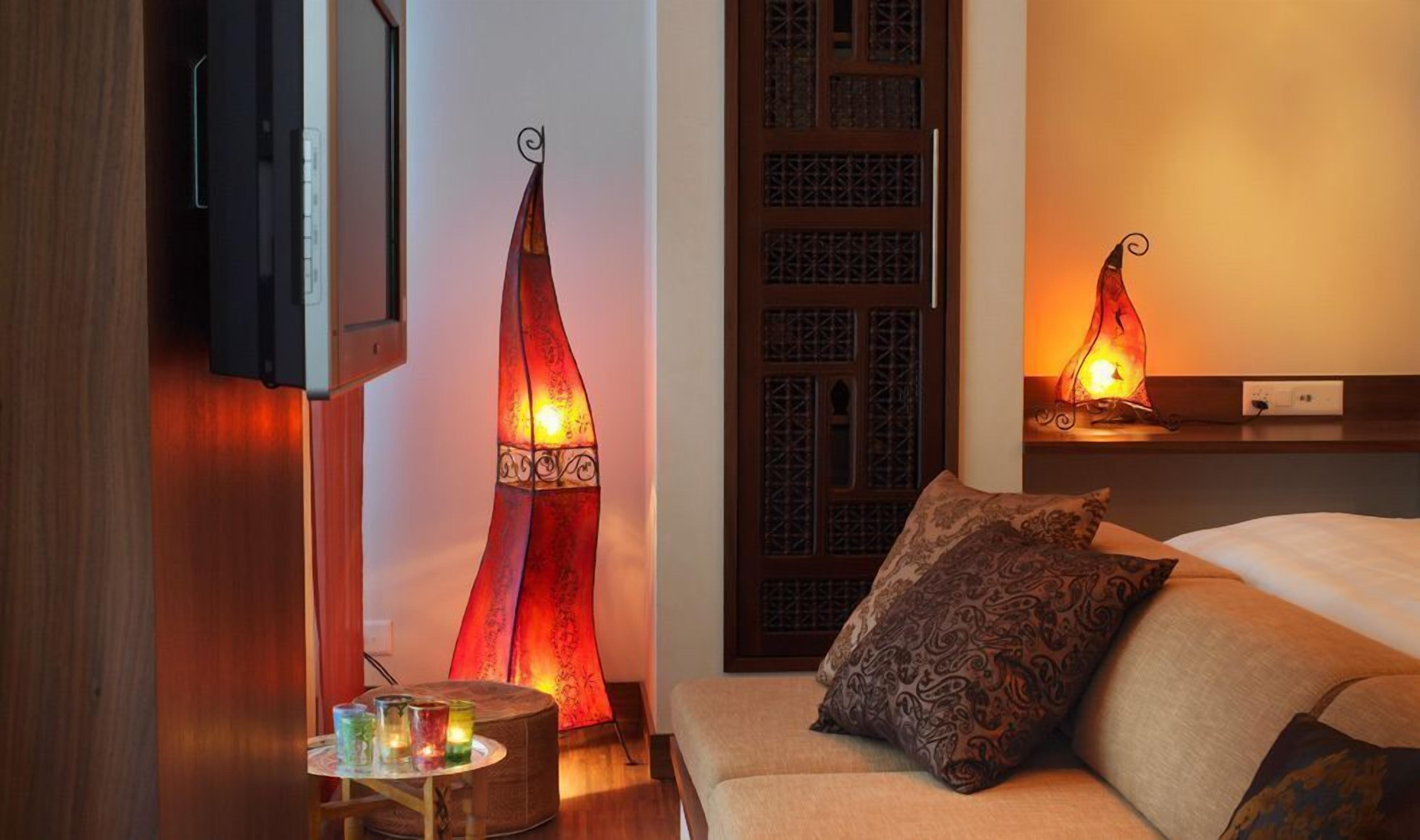 A hotel room with a bed, a TV mounted on the wall, decorative lamps, and a small table with candles.