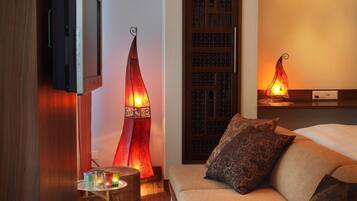 A hotel room with a bed, a TV mounted on the wall, decorative lamps, and a small table with candles.