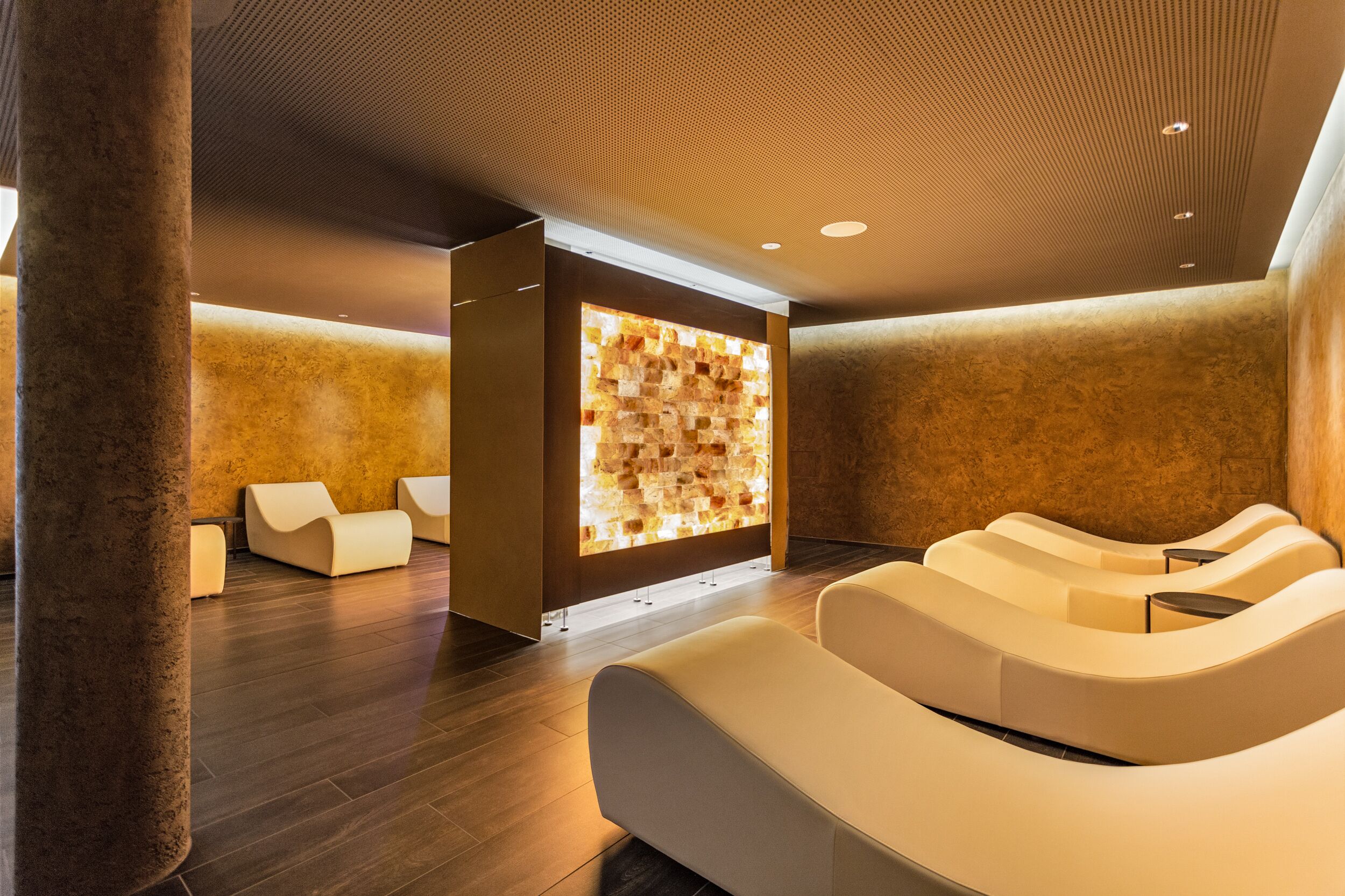 A modern spa area with a stone wall, cushioned seating, and a wooden ceiling.