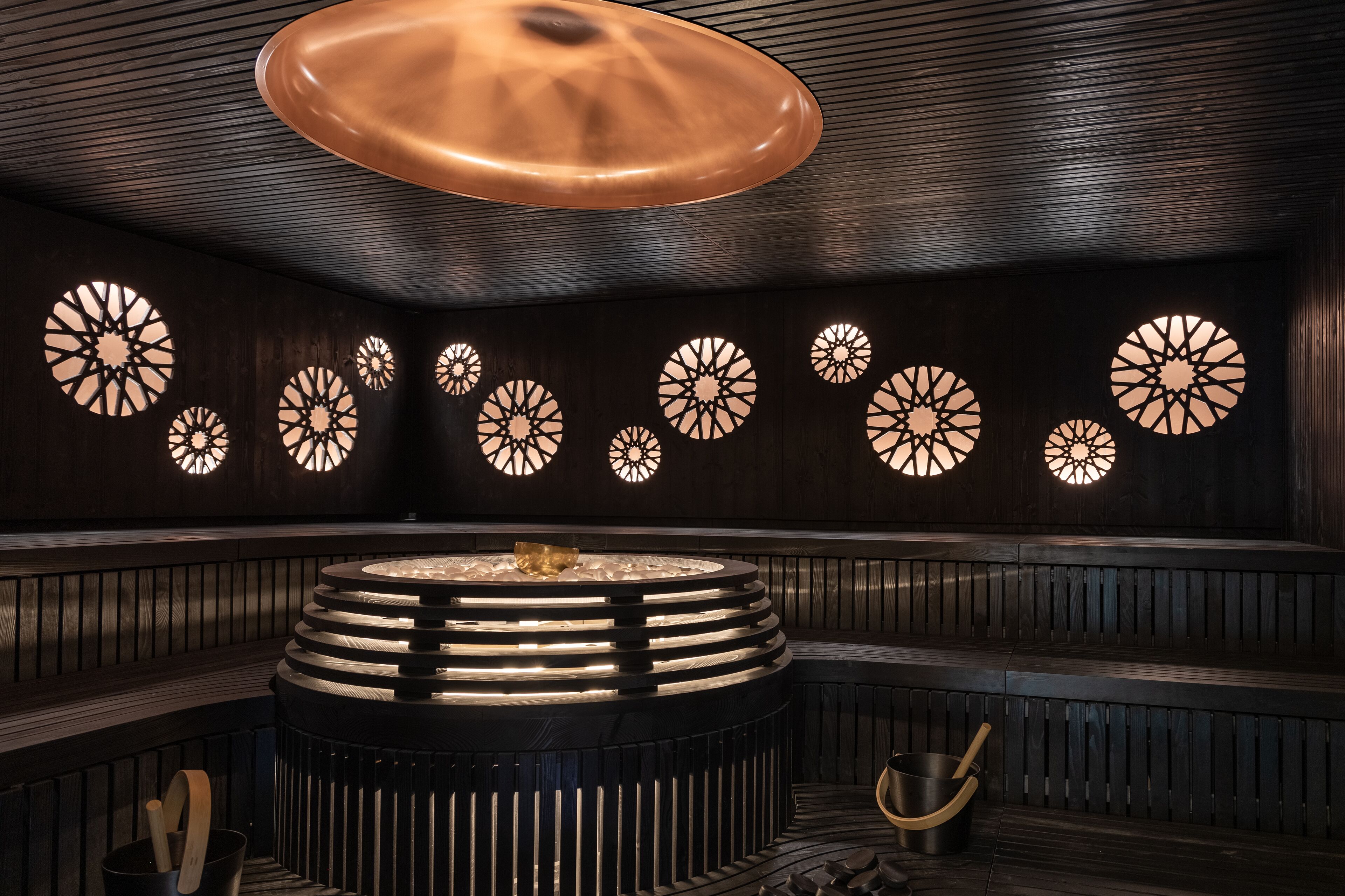 A modern interior with a central circular seating area, wooden paneling, and decorative wall lights.