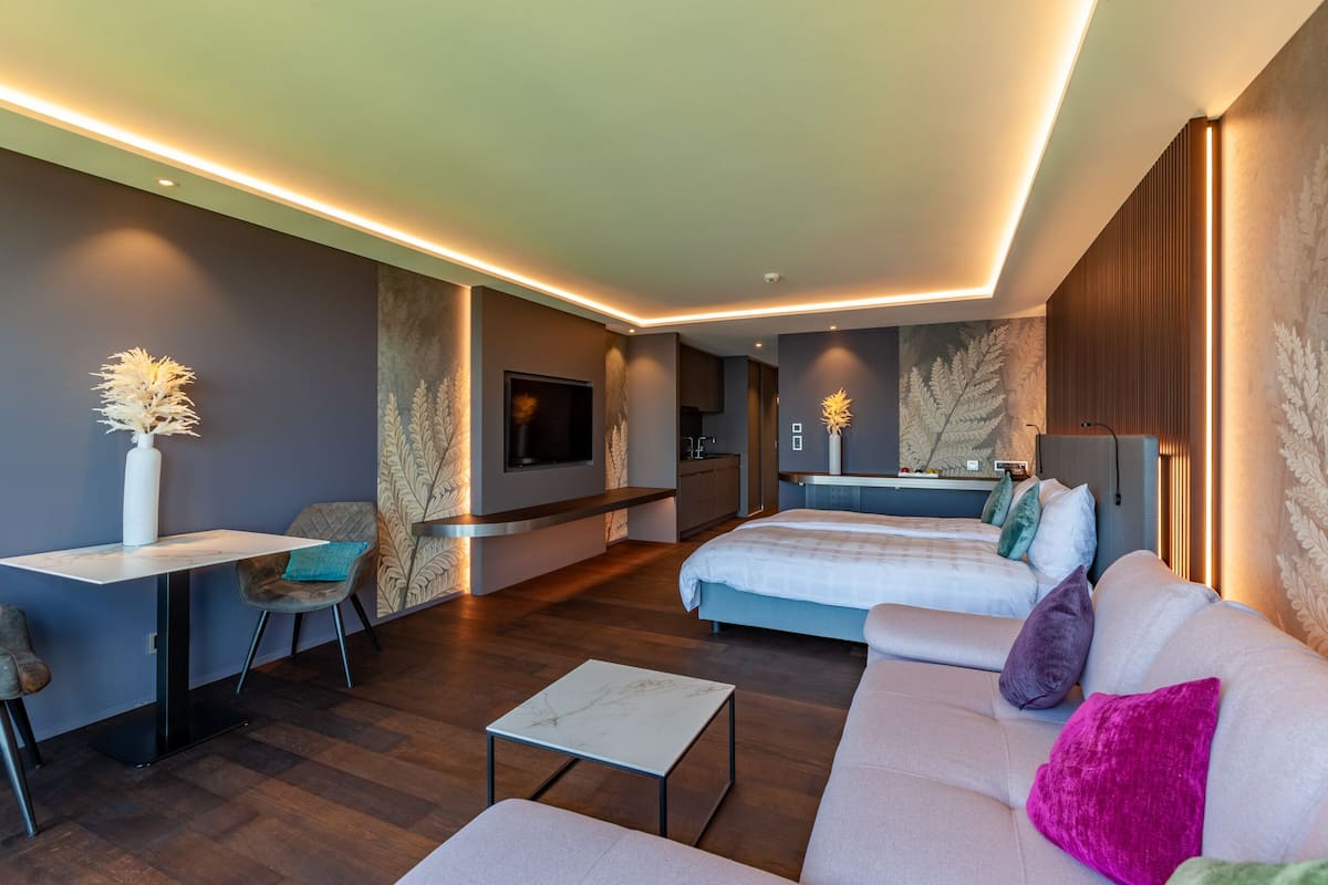 Ein modernes Hotelzimmer mit einer Couch, zwei Betten, einem Esstisch und einer kleinen Küchenzeile.
