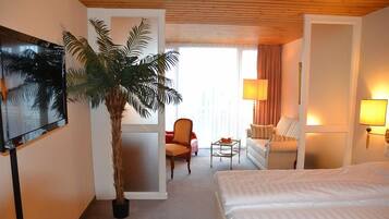 A hotel room with a bed, a sofa, a chair, a TV, a lamp, and a plant.