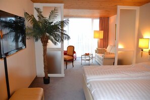 A hotel room with a bed, a sofa, a chair, a TV, a lamp, and a plant. - T3 Alpenhotel Flims (Flims)