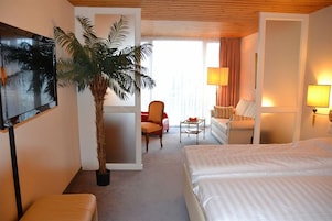 Una habitación de hotel con cama, sofá, sillón, televisor, lámpara y planta en maceta.