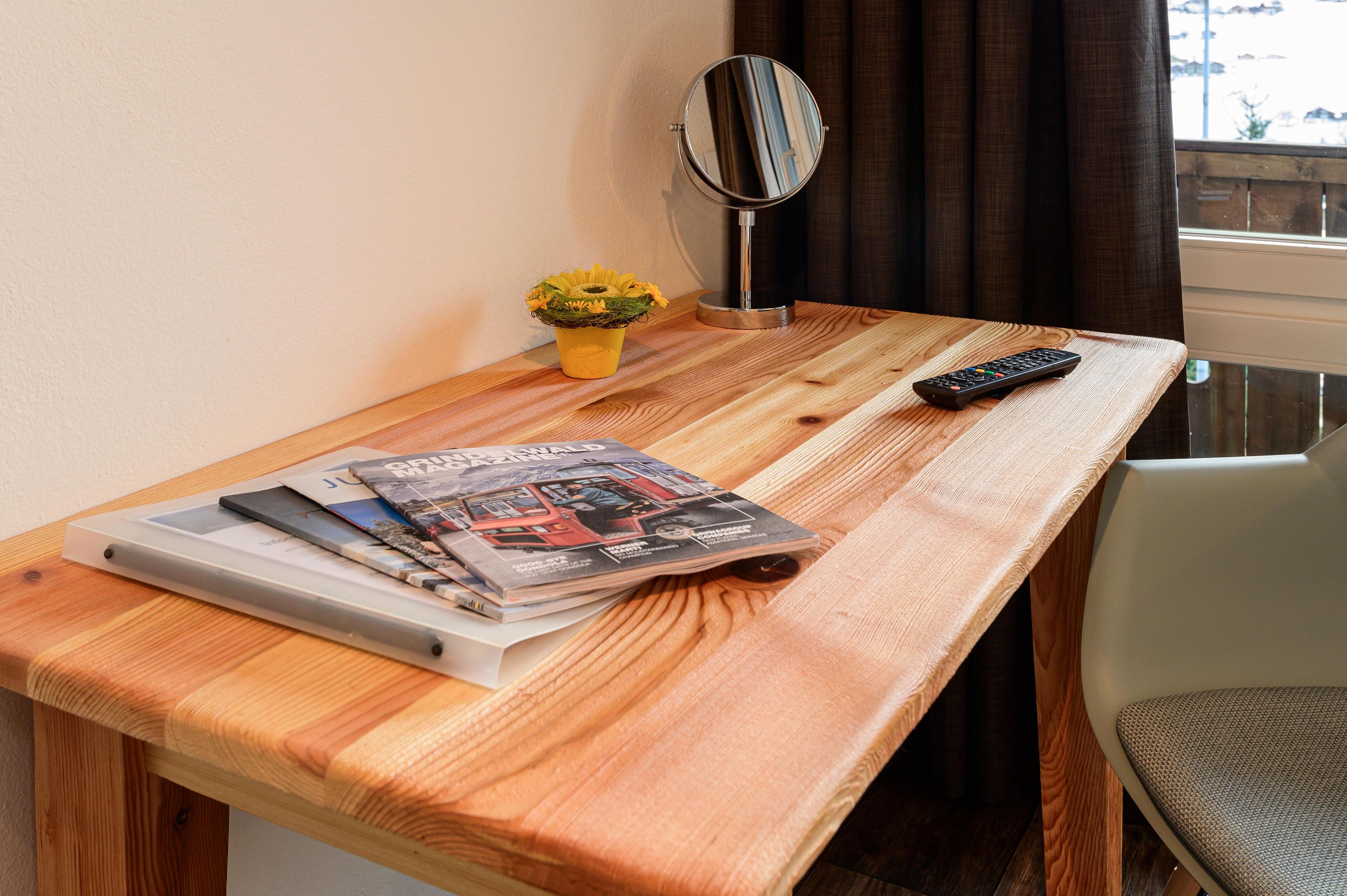 A wooden table with a remote control, a mirror, a small plant, and magazines.