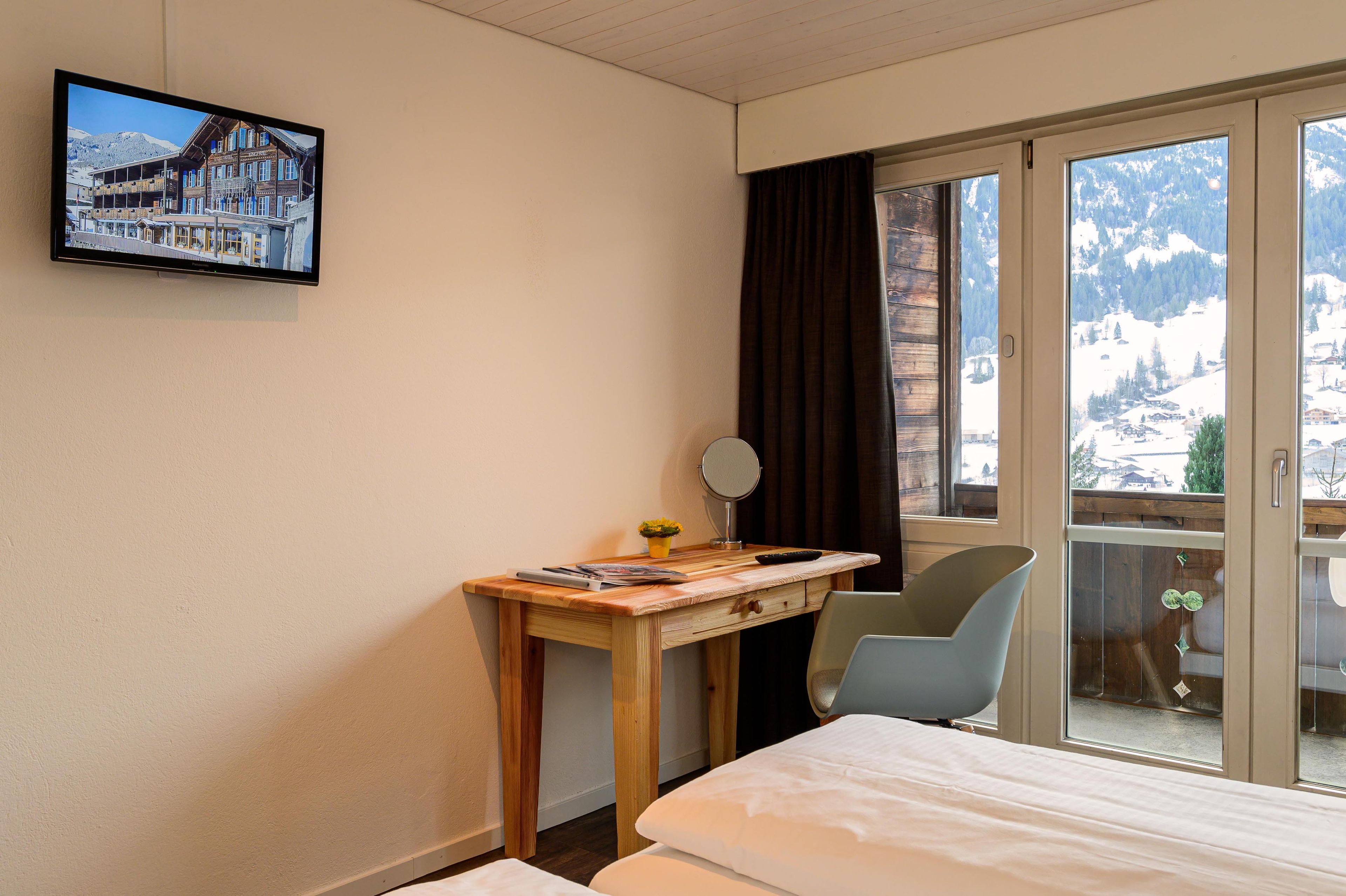 Habitación de hotel con cama, escritorio con computadora, silla, ventana con vista a montañas y televisión en la pared.