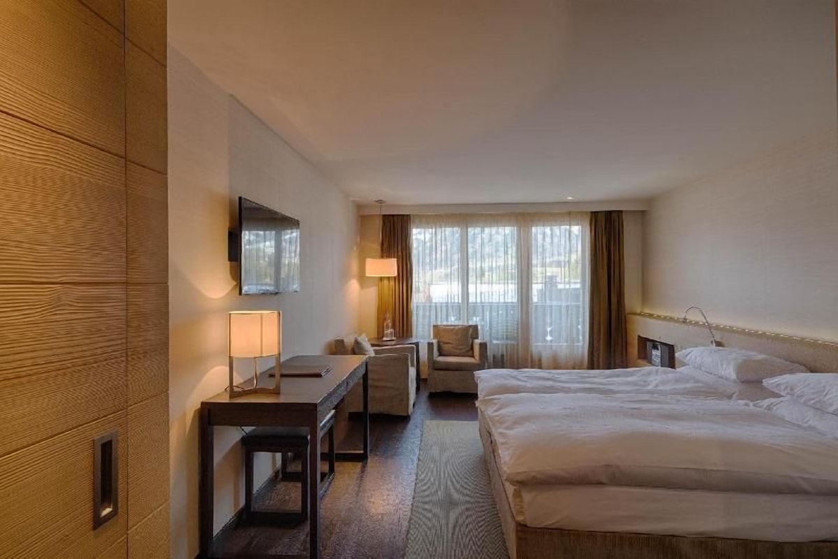 A hotel room with a bed, a desk, a chair, a TV, and a window with curtains.