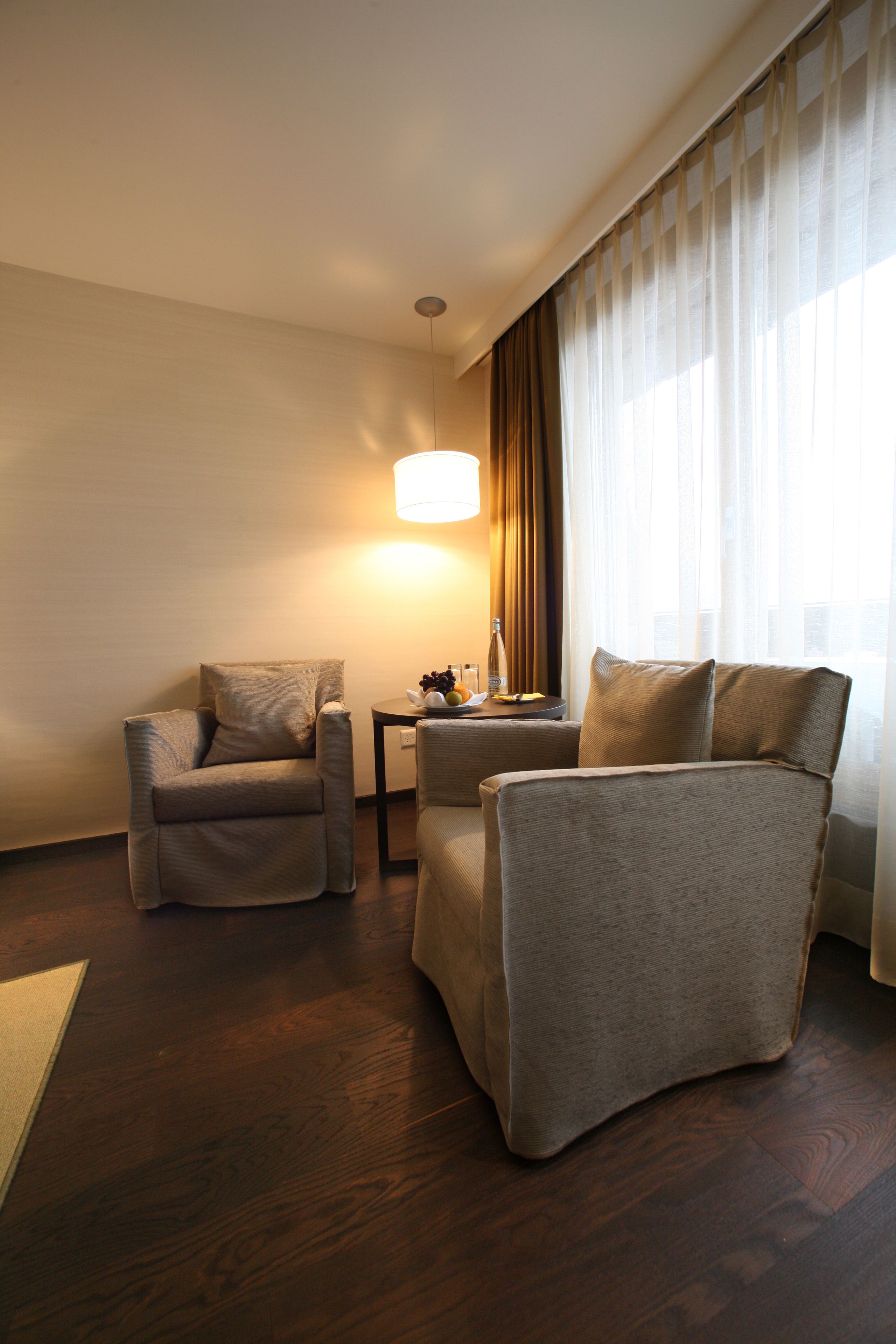 A hotel room with two armchairs, a small table with a lamp, and a window with curtains.