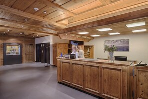 A reception area with wooden paneling, a reception desk, a counter with a vase of flowers, and a painting on the wall.