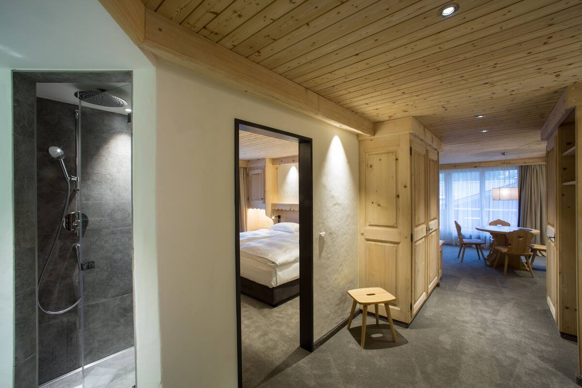 Una habitación de hotel moderna con ducha, cama, un taburete pequeño y una zona de comedor con mesa y sillas.