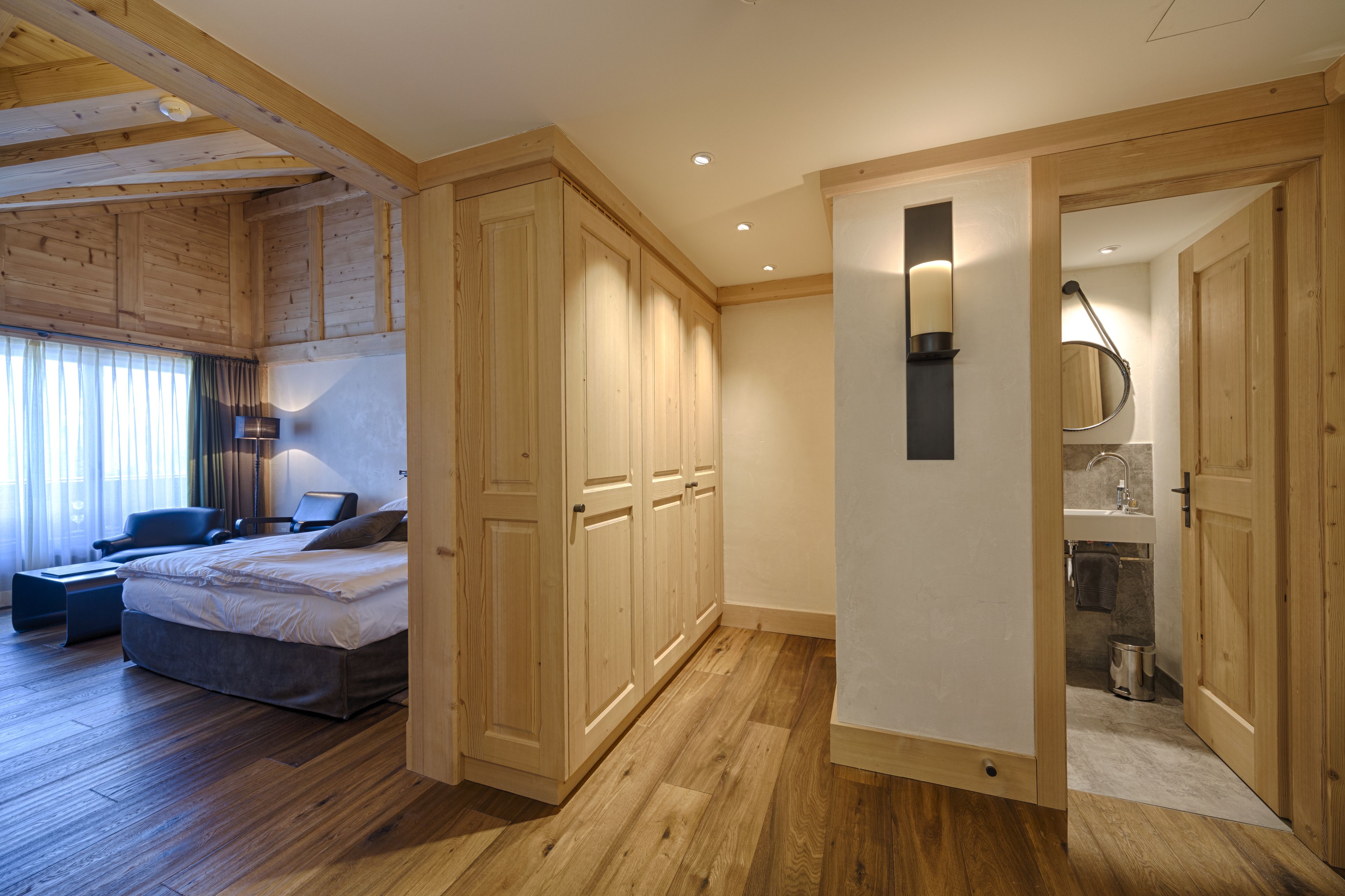 Ein Schlafzimmer mit Bett, Schreibtisch und Stuhl. Es gibt einen Holzschrank und ein Badezimmer mit Waschbecken und Spiegel.