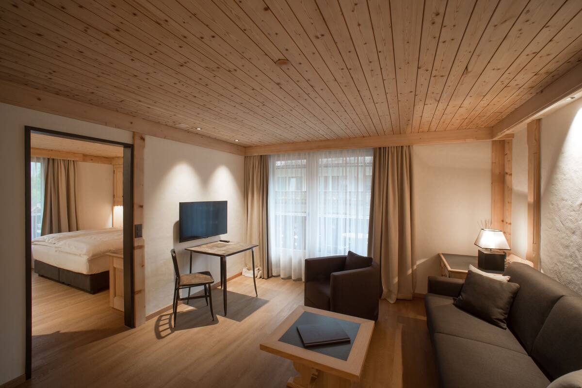 Una habitación de hotel moderna con techo de madera, una cama, un escritorio con silla, un sofá y un televisor.