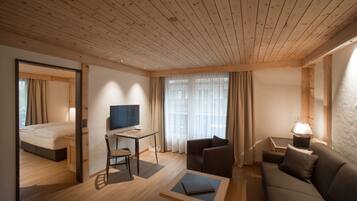 A modern hotel room with a wooden ceiling, a bed, a desk with a chair, a sofa, and a TV.