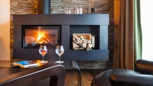 Una sala de estar moderna con una pared de piedra, una chimenea, dos copas de vino y un libro sobre una mesa.