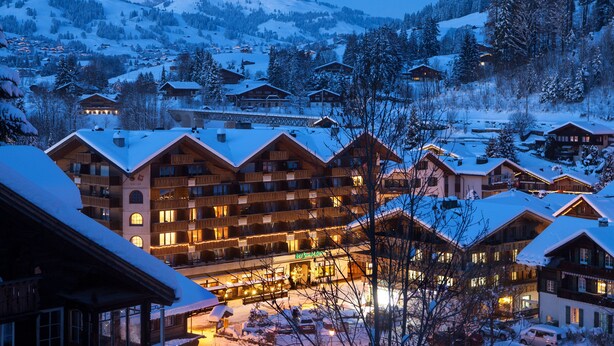 Un complejo turístico cubierto de nieve con varias edificaciones, incluyendo un gran edificio principal con balcones y una zona de restaurante.