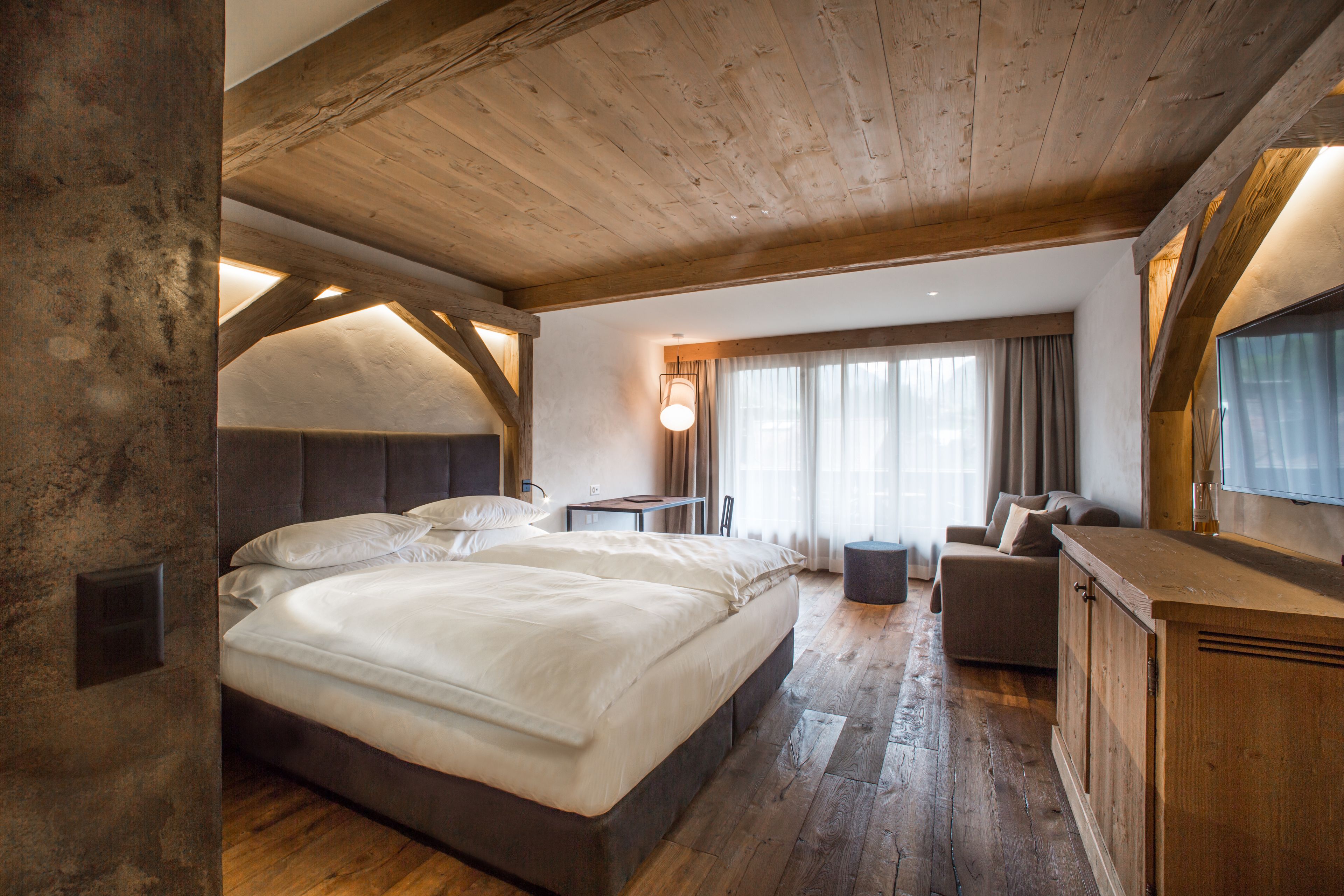 A bedroom with a large bed, a sofa, a TV, and a wooden ceiling.