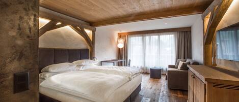 A bedroom with a large bed, a sofa, a TV, and a wooden ceiling.
