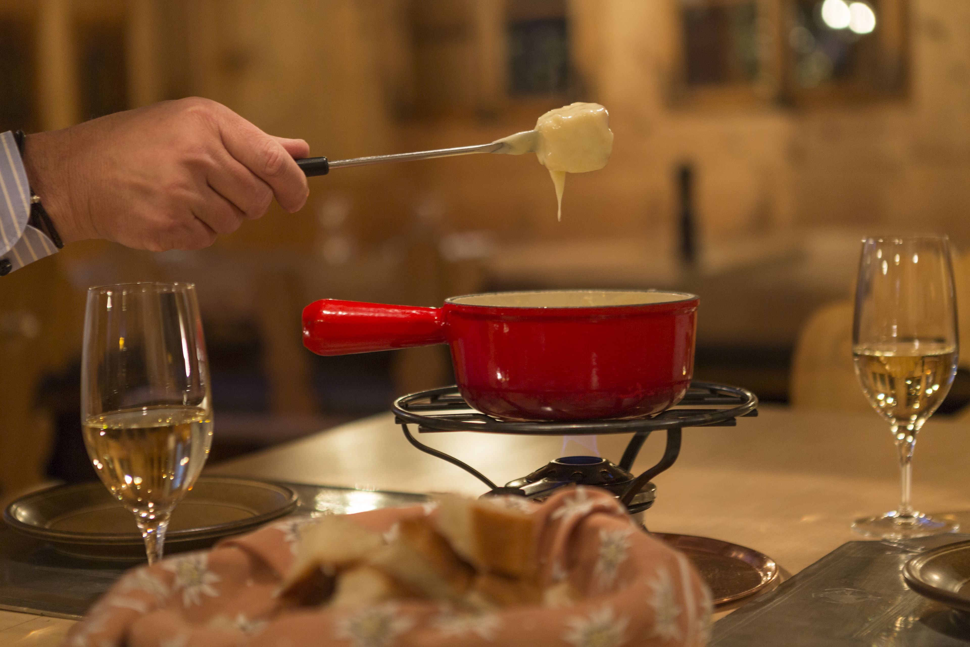 A red pot on a portable stove with a spoon holding a creamy substance. Two glasses of white wine are on the table.