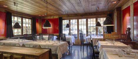 A restaurant with wooden ceiling and red walls, tables set with white tablecloths and chairs.