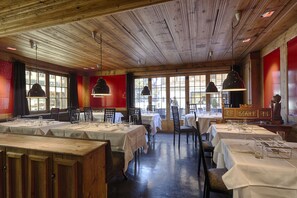 Restaurante com teto de madeira e paredes vermelhas, mesas com toalhas brancas e cadeiras.