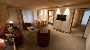 Quarto de hotel com teto de madeira, sofá, mesa de jantar, televisão e espelho.