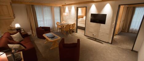 A hotel room with a wooden ceiling, a sofa, a dining table, a TV, and a mirror.