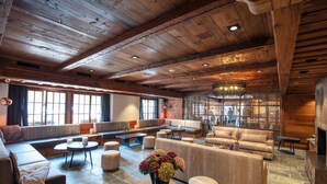 Amplia sala de estar con techos de madera, asientos cómodos, chimenea y ventanas grandes que dejan entrar luz natural.