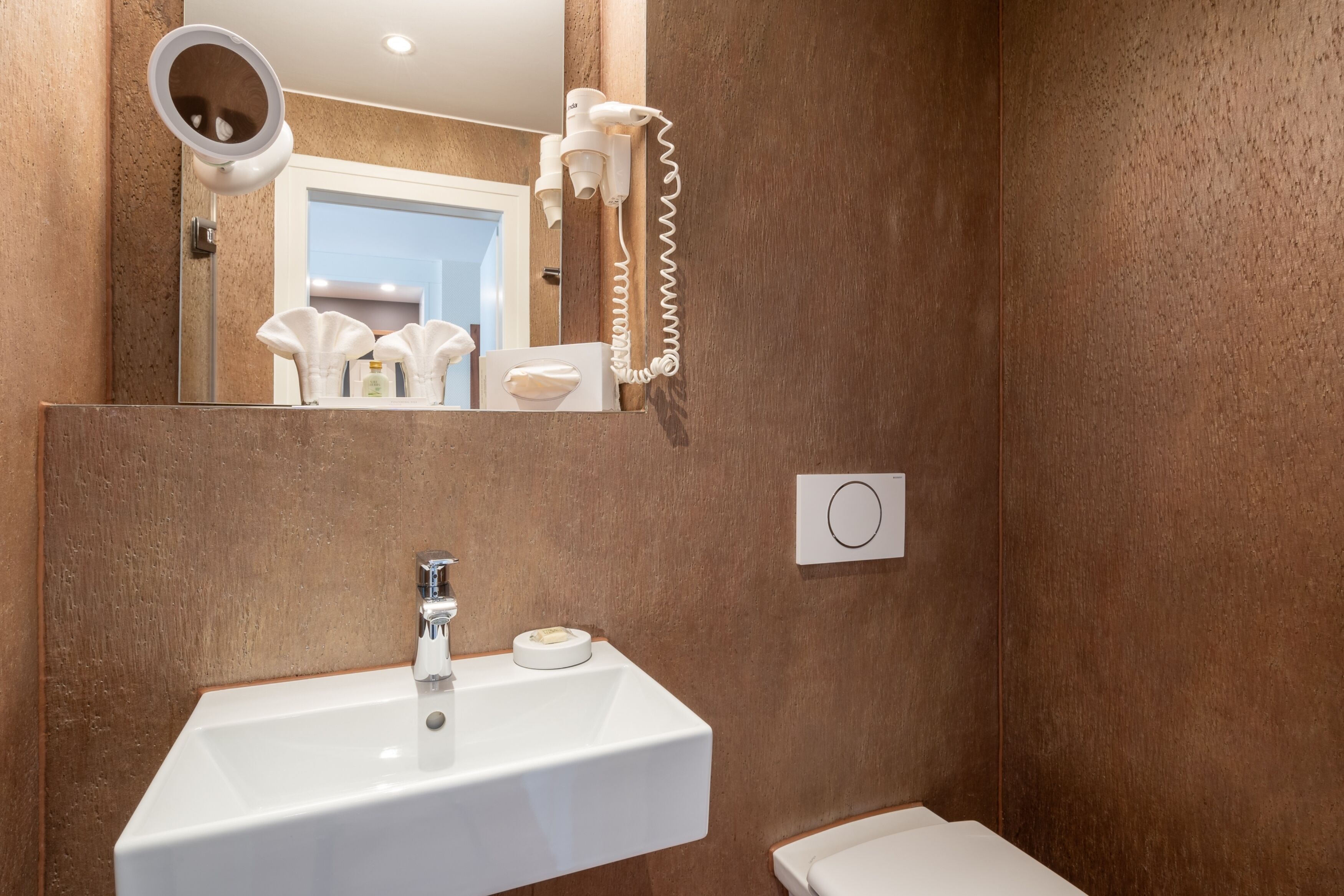 A bathroom with a white sink, a mirror, and a hairdryer mounted on the wall.