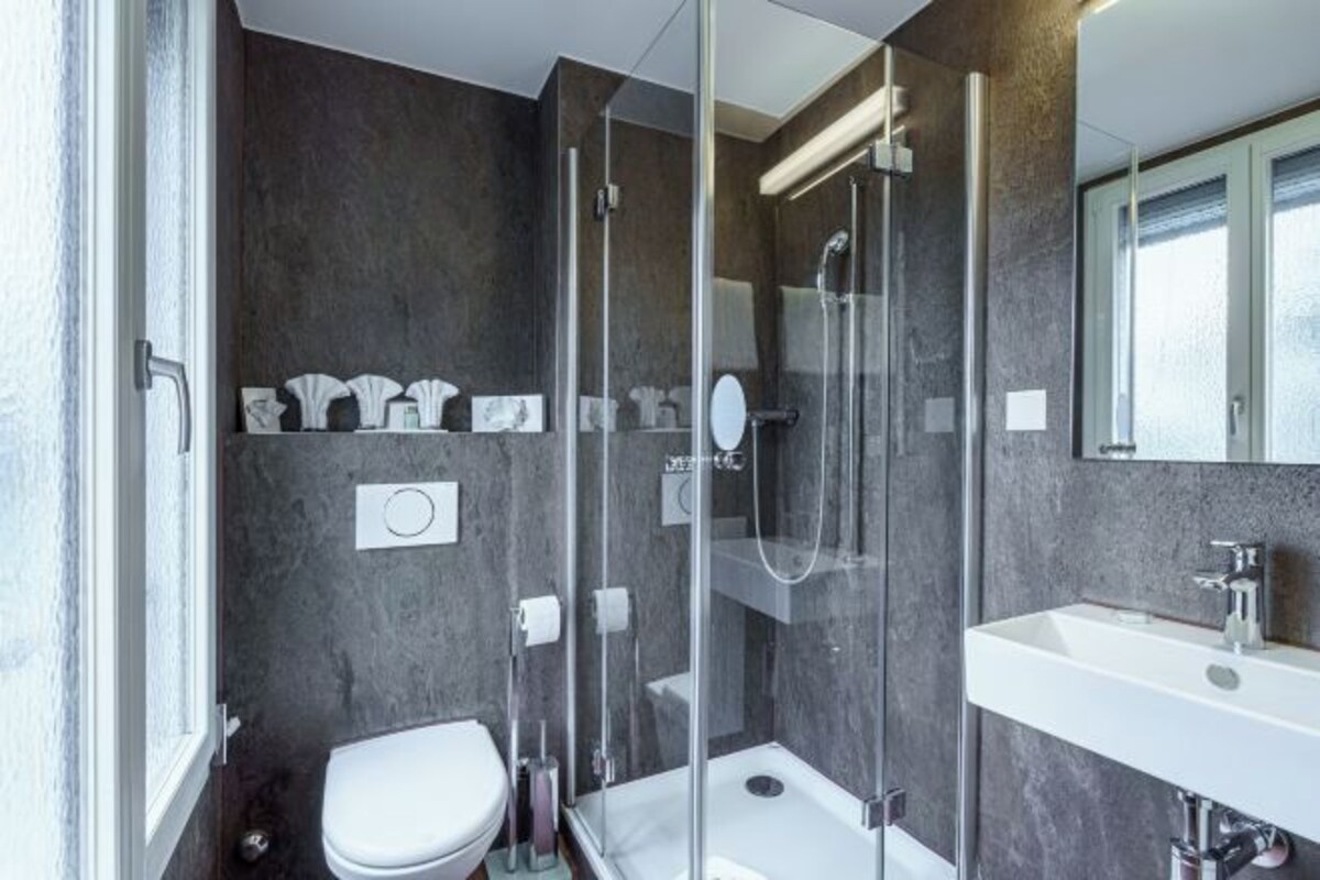 A modern bathroom with a glass-enclosed shower, a white sink, and a toilet.