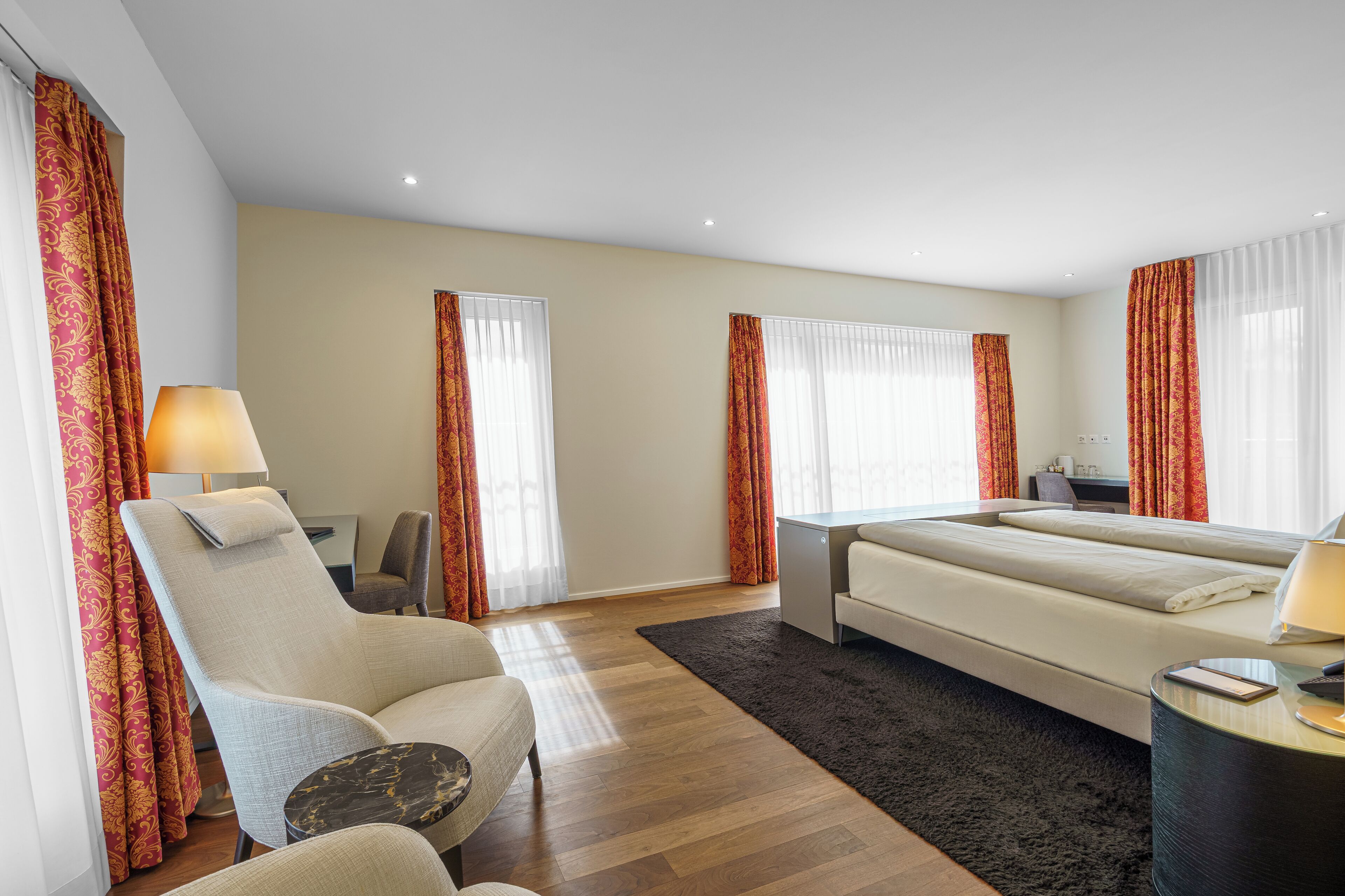 A hotel room with a bed, a chair, a desk, and a lamp.