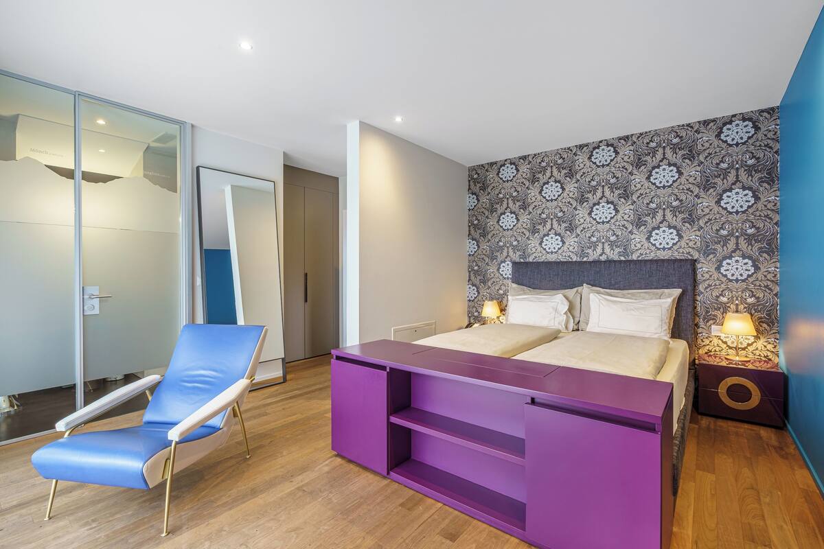 A modern bedroom with a bed, a blue chair, and a purple console.