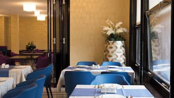 A restaurant with tables set for dining, blue chairs, and a large vase with flowers.