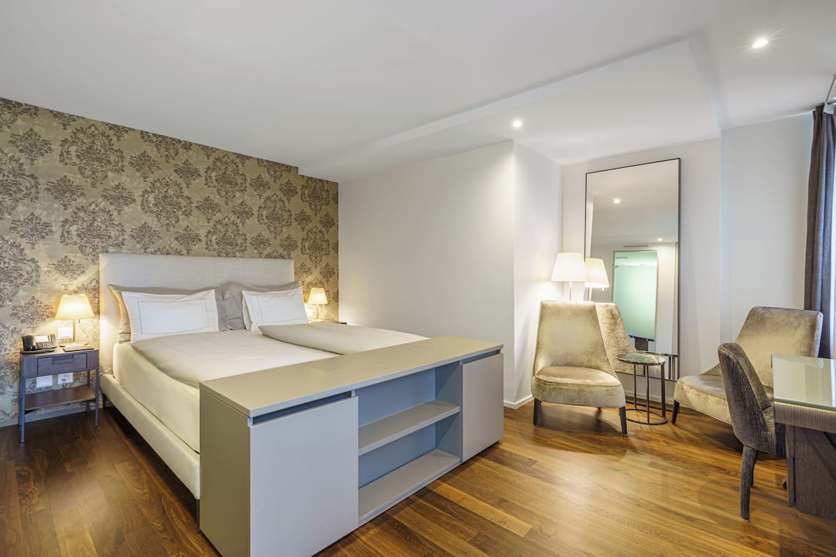 A modern hotel room with a large bed, a chair, a small table, and a mirror.