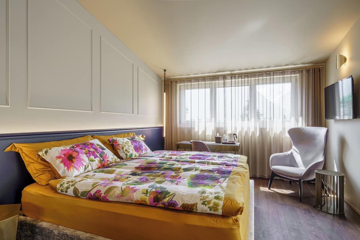 A hotel room with a bed, a desk, a chair, and a TV.
