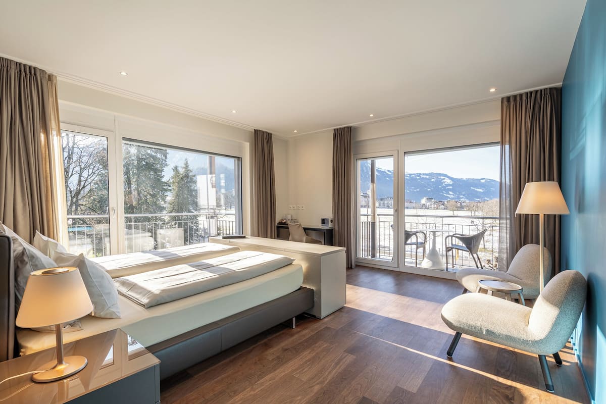 A modern hotel room with a large bed, a desk, a chair, and a balcony with a view.