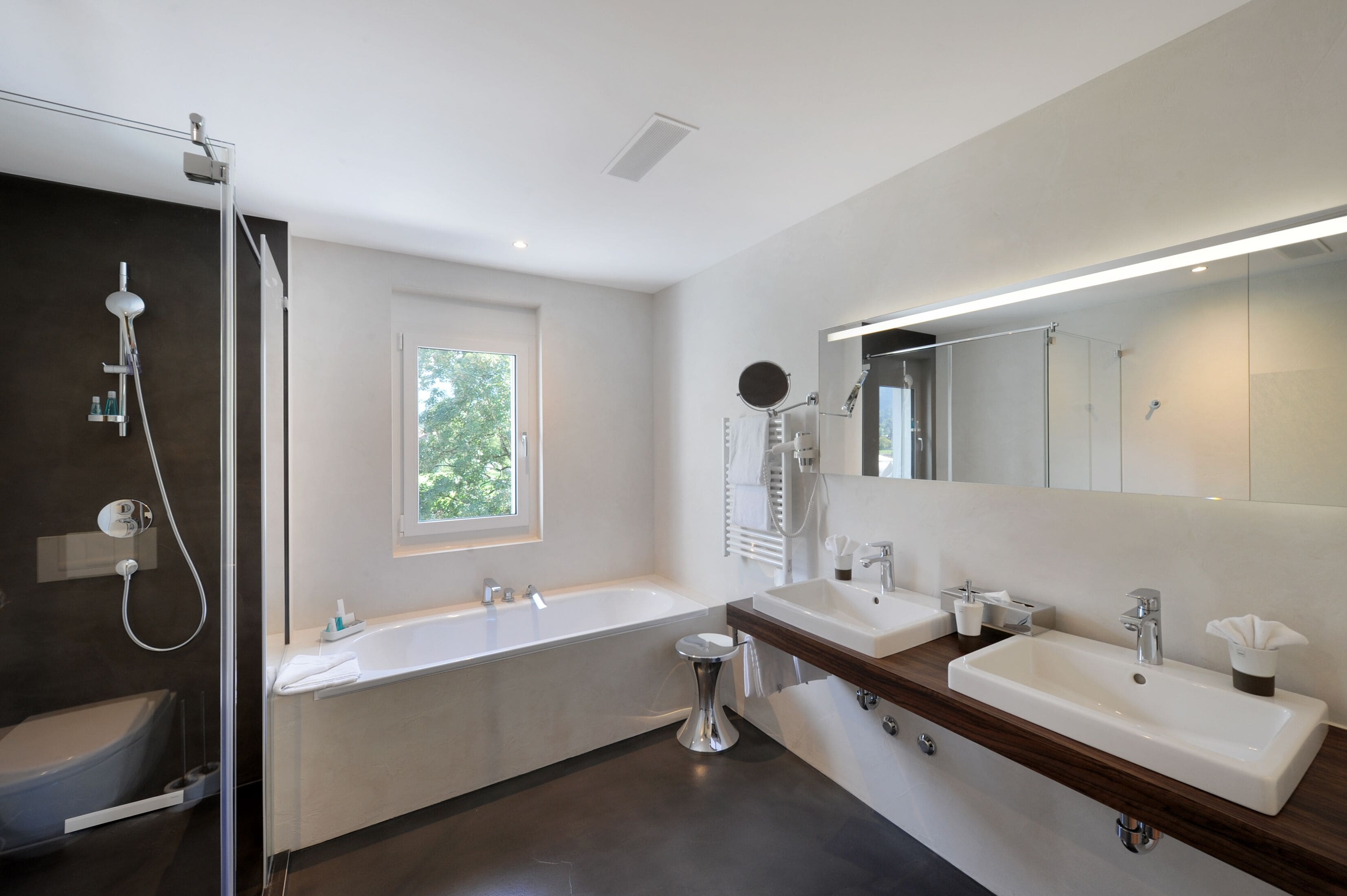 A modern bathroom with a bathtub, two sinks, a large mirror, and a shower area.
