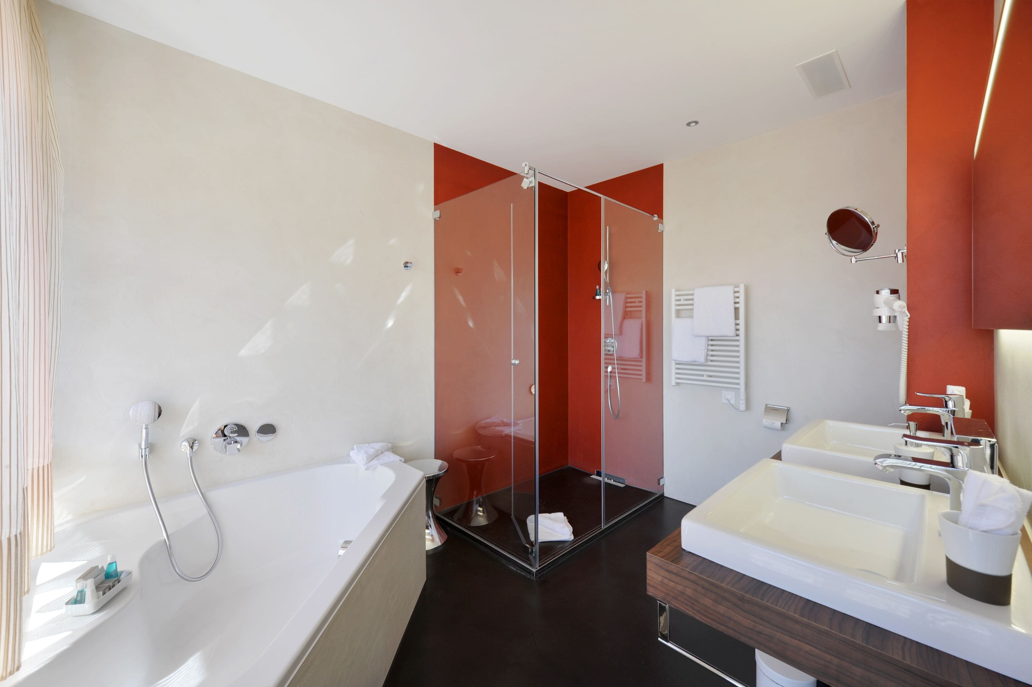 A modern bathroom with a bathtub, two sinks, a glass-enclosed shower, and a towel rack.
