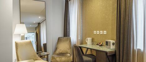 A hotel room with a desk, two chairs, a lamp, a coffee maker, and a radio.