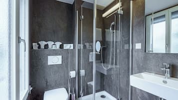 Ein modernes Badezimmer mit einer gläsernen Duschkabine, einem weißen Waschbecken und einer Marmorwand.