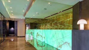 Un área de recepción moderna con un mostrador de mármol, una instalación de luces geométricas en la pared y un piso pulido.
