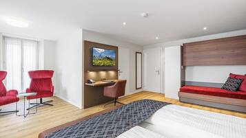 A modern hotel room with a bed, a desk, two red chairs, a TV, and a red sofa.