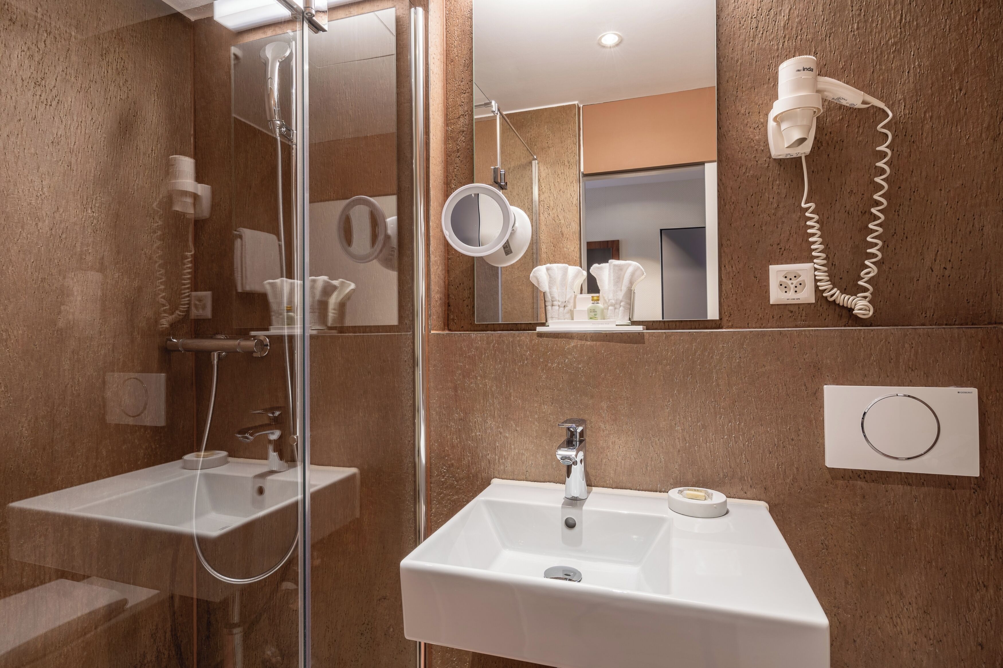 A modern bathroom with a glass shower enclosure, two sinks, a hairdryer, and a mirror.