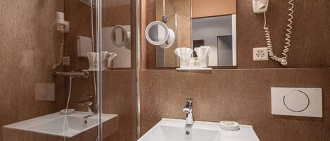 A modern bathroom with a glass shower enclosure, two sinks, a hairdryer, and a mirror.